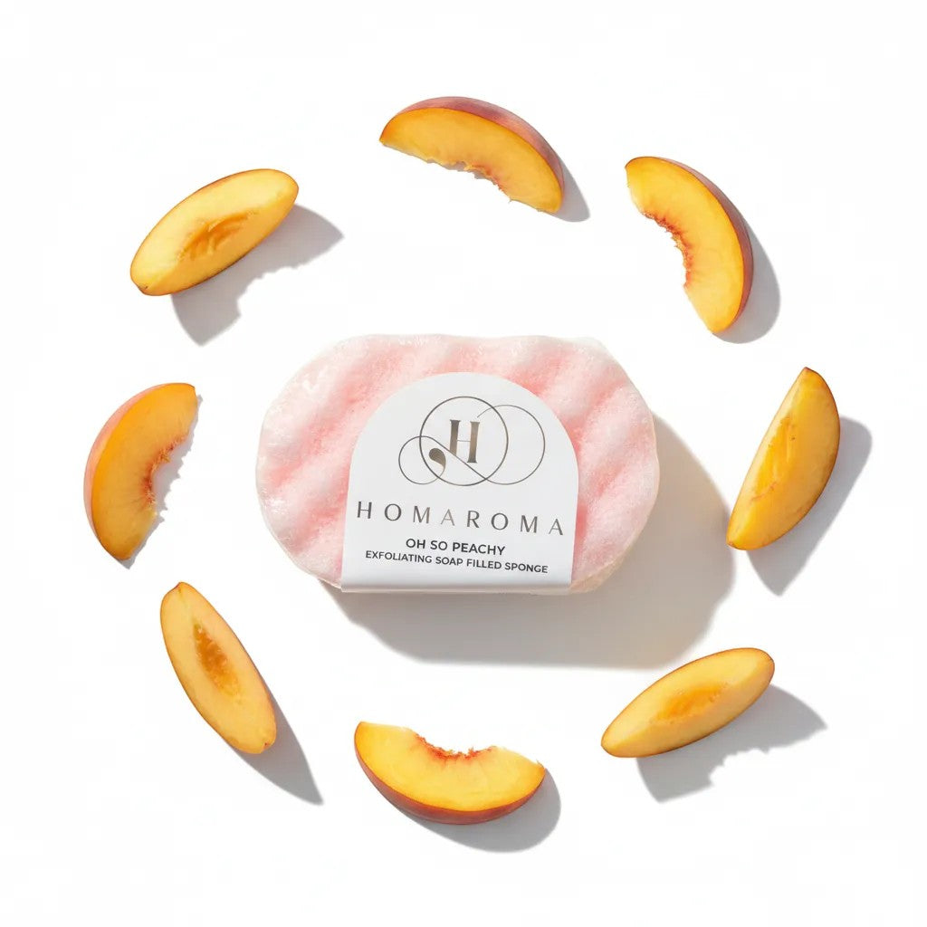 Homaroma Oh So Peachy exfoliating soap filled sponge, pink with wavy texture, surrounded by peach slices.