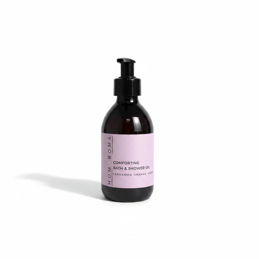Homaroma Comforting Bath & Shower Oil in a dark amber glass bottle with a black pump dispenser and soft pink label.