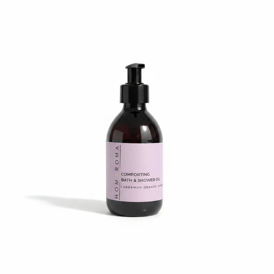 Homaroma Comforting Bath & Shower Oil in a dark amber glass bottle with a black pump dispenser and soft lilac label.