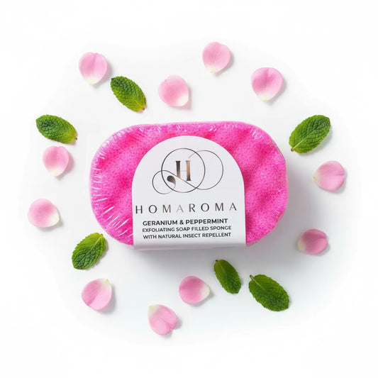 Homaroma pink exfoliating soap-filled sponge with Geranium & Peppermint and natural insect repellent, surrounded by rose petals and mint leaves.