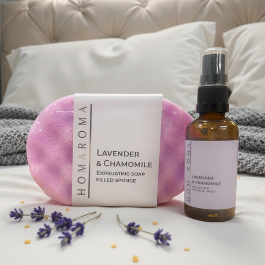 Homaroma Lavender & Chamomile Pillow Ritual Trio set with exfoliating soap sponge and pillow mist on a bed.